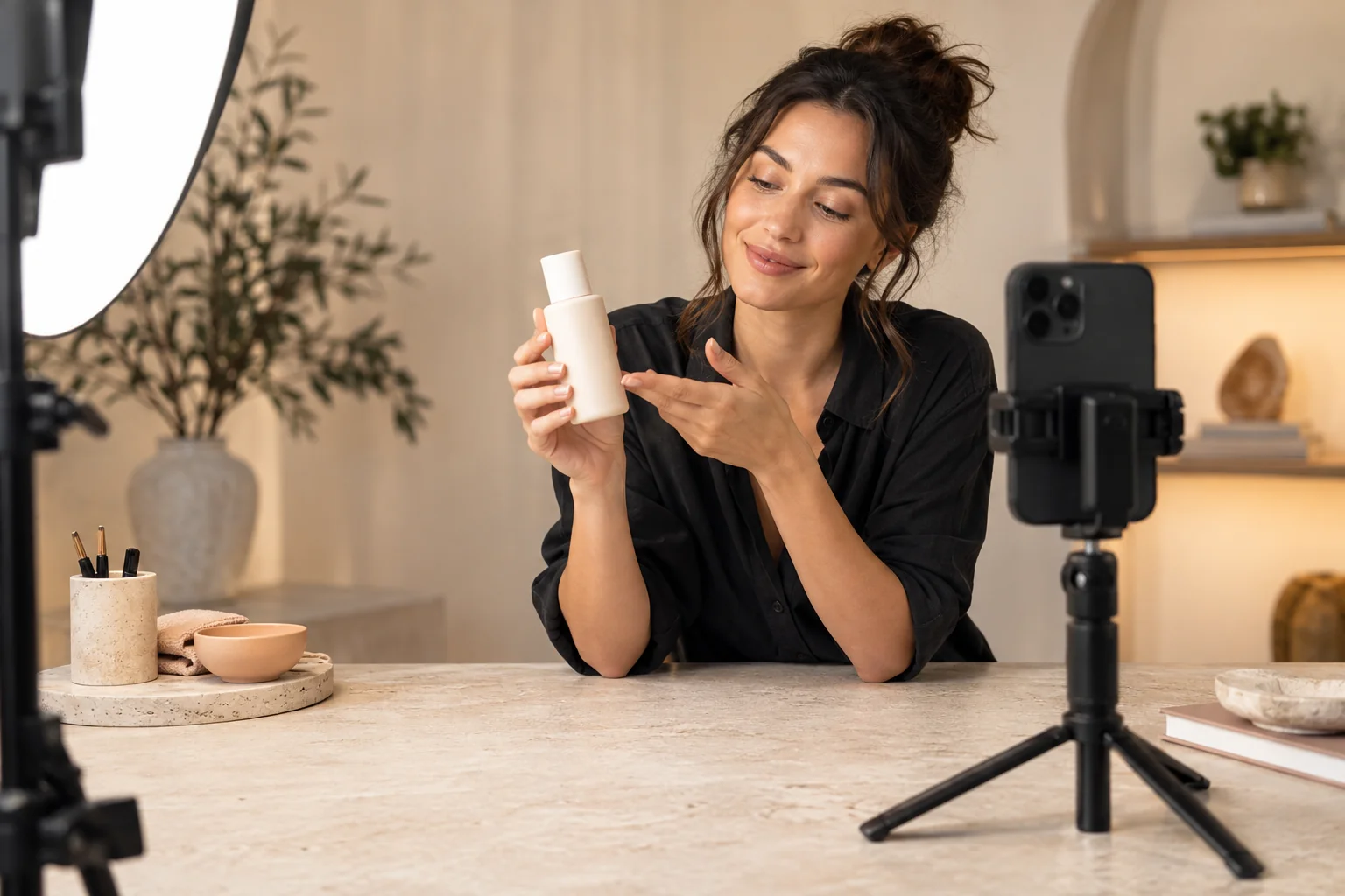 A woman demonstrates an unlabeled bottle beside a smartphone in a bright studio.
